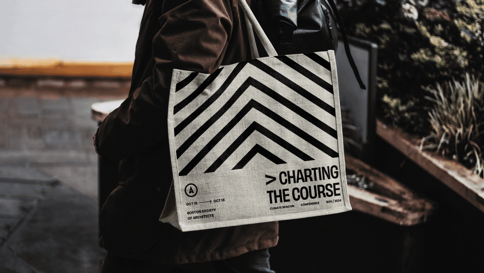 Person carrying a tote bag with black geometric lines and the text "Charting the Course - North Carolina State University College of Design - Oct 11 - Oct 13.
