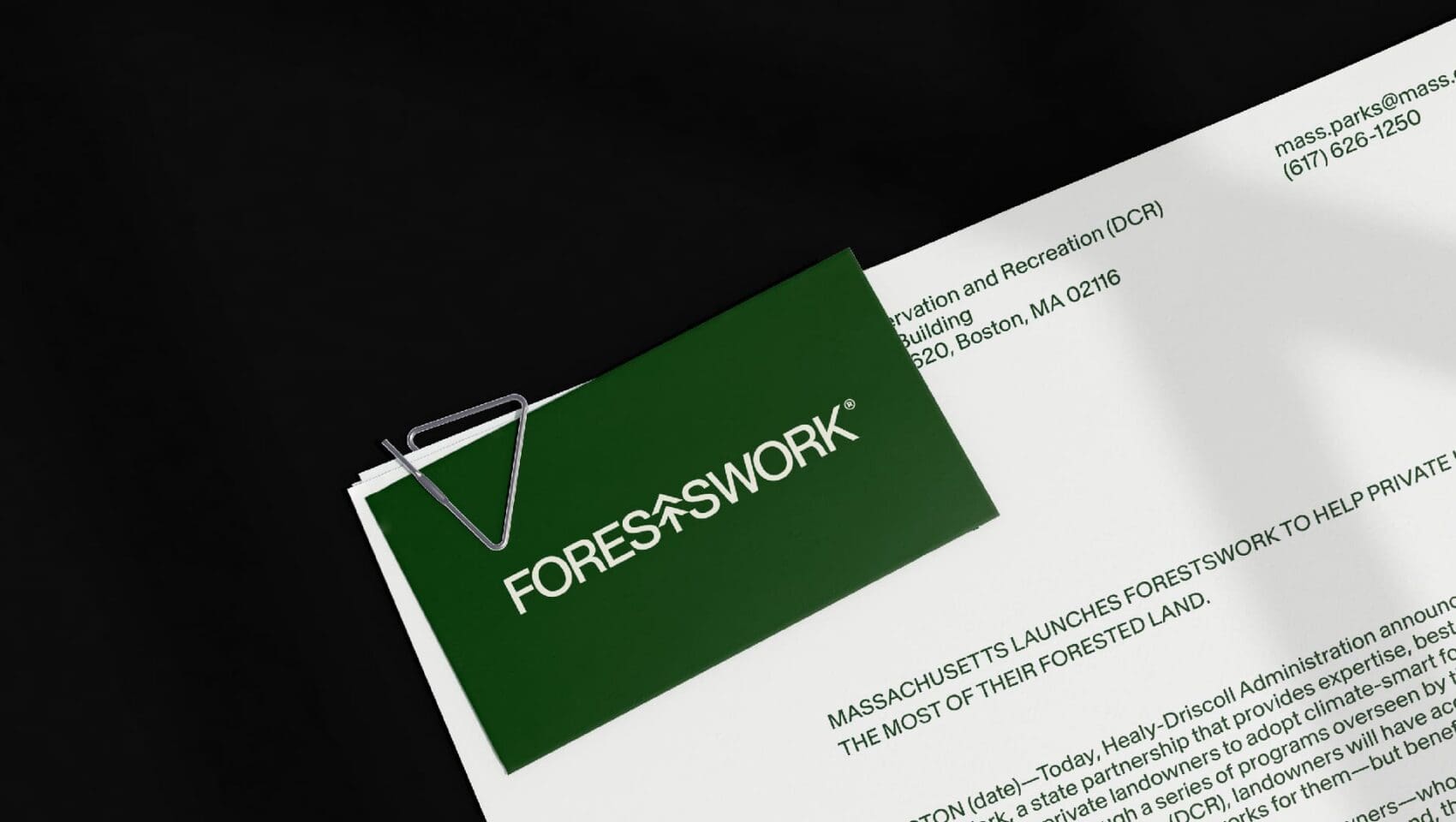 A green folder with "FORESTS+WORK" on it is clipped to a document titled "Massachusetts Launches Forests+Work to Help Private..." from the Department of Conservation and Recreation.