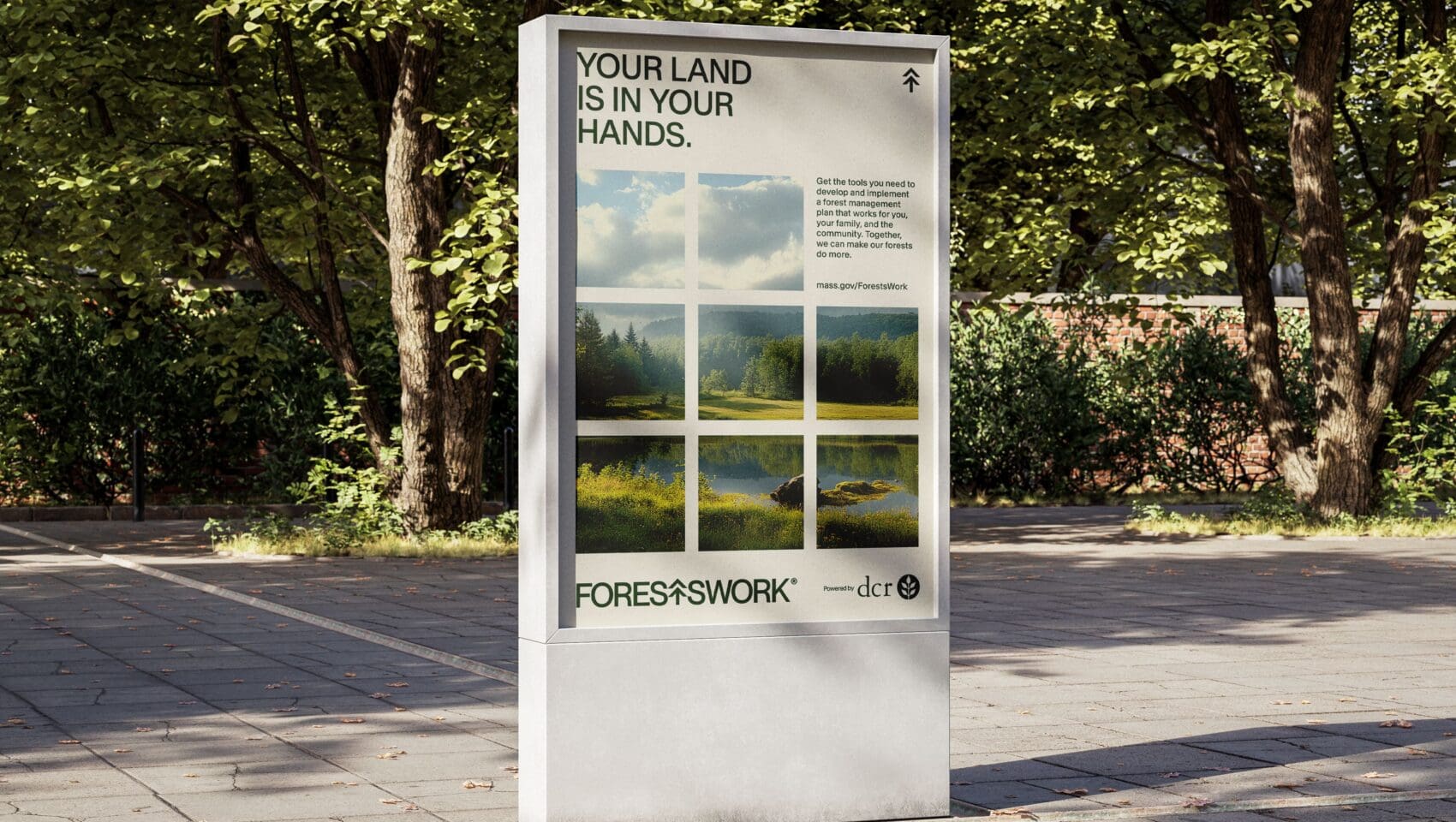 Outdoor advertising board showing a scenic landscape photo grid with the text "Your land is in your hands" and "Forest & Work" logo, set against a backdrop of trees and paved ground.