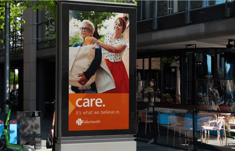Outdoor advertisement featuring two people smiling and carrying laundry, with the text "care. It's what we believe in." and a logo for #allonhealth.