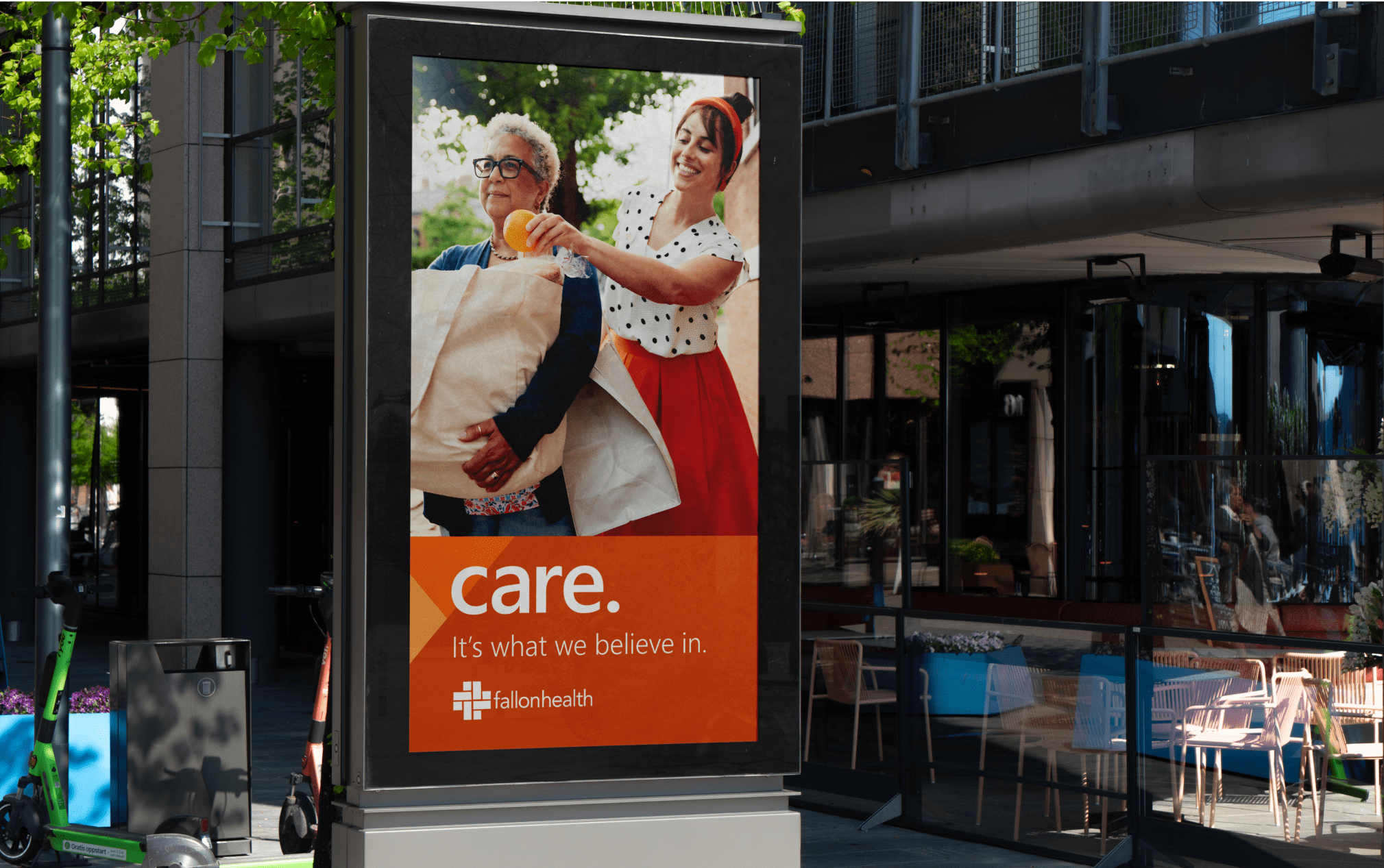 Outdoor advertisement featuring two people smiling and carrying laundry, with the text "care. It's what we believe in." and a logo for #allonhealth.