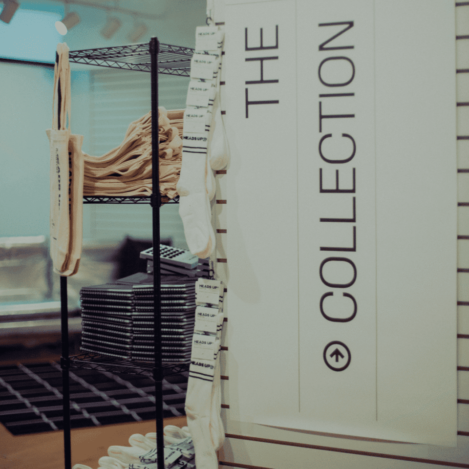 Shelves with tote bags, socks, and stacked items next to a wall sign reading "THE COLLECTION" with an arrow.