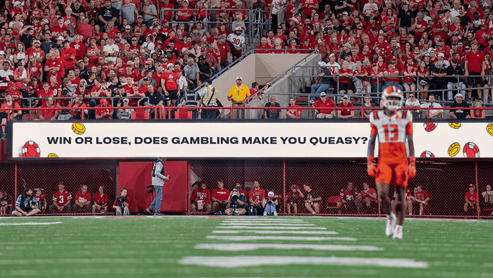 A football player stands on the field in front of a crowd and a stadium sign that reads, "WIN OR LOSE, DOES GAMBLING MAKE YOU QUEASY?.