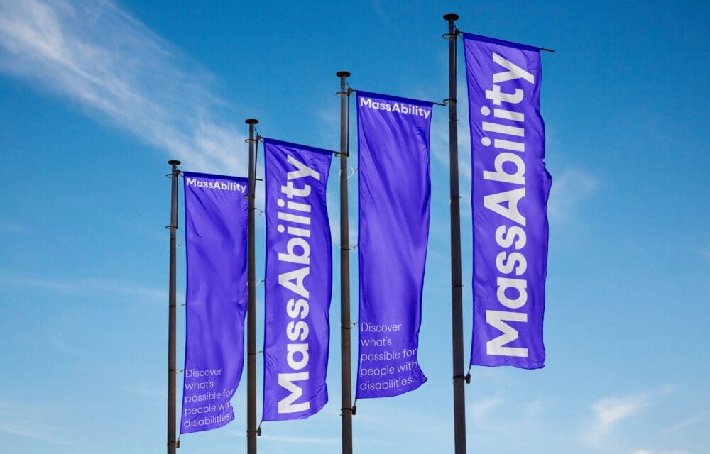 Four purple flags with "MassAbility" and a slogan fly against a blue sky.