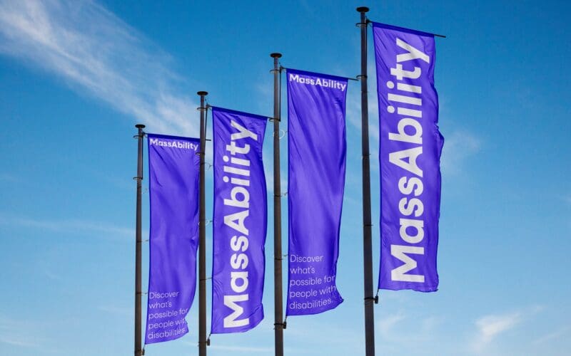 Four purple flags with "MassAbility" and a slogan fly against a blue sky.
