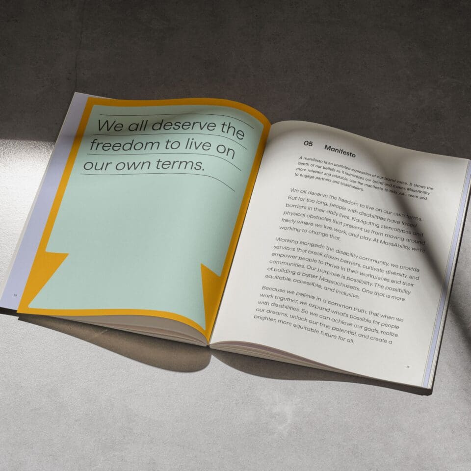 Open book on a concrete surface, featuring a page with large text reading, "We all deserve the freedom to live on our own terms," alongside a manifesto. Shadows cast across the pages.