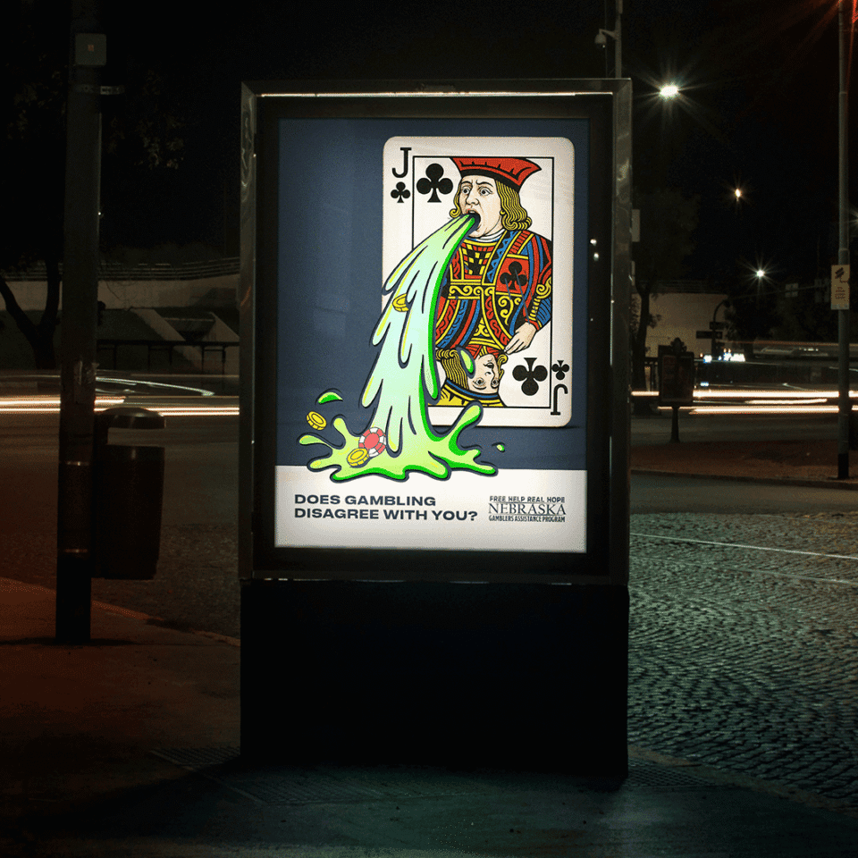 A bus stop ad at night shows a cartoon Jack of Clubs vomiting chips and dice, with the text, "DOES GAMBLING DISAGREE WITH YOU?" and a Nebraska problem gambling helpline.