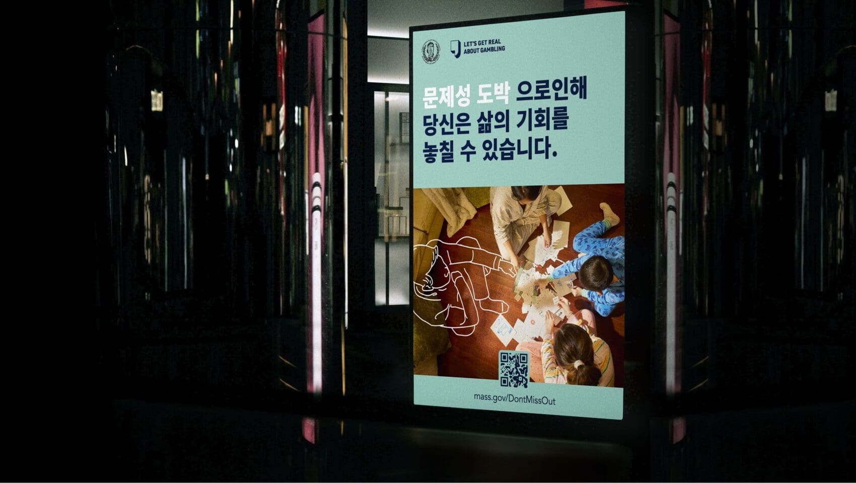 A digital sign displays a warning in Korean and English about missing life opportunities, with an overhead photo of people playing cards on the floor and a QR code linking to mass.gov/DontMissOut.
