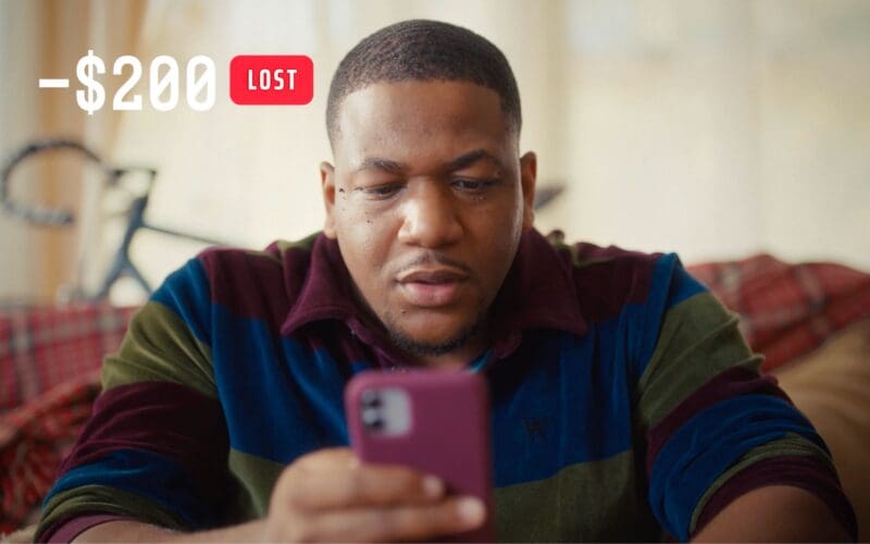 A man looks at his phone with a serious expression; a “$200 lost” notification appears above him.