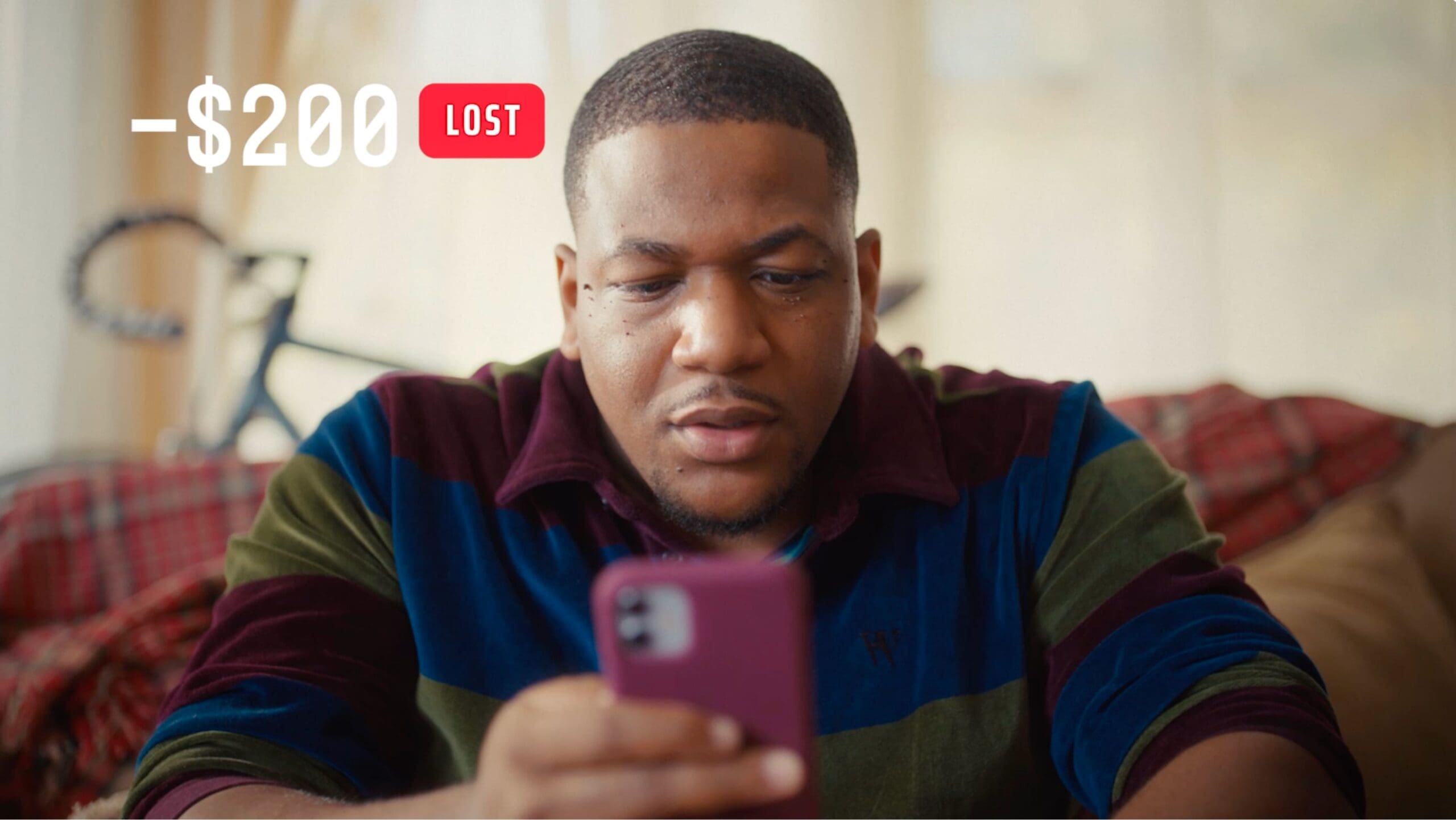 A man looks at his phone with a serious expression; a “$200 lost” notification appears above him.